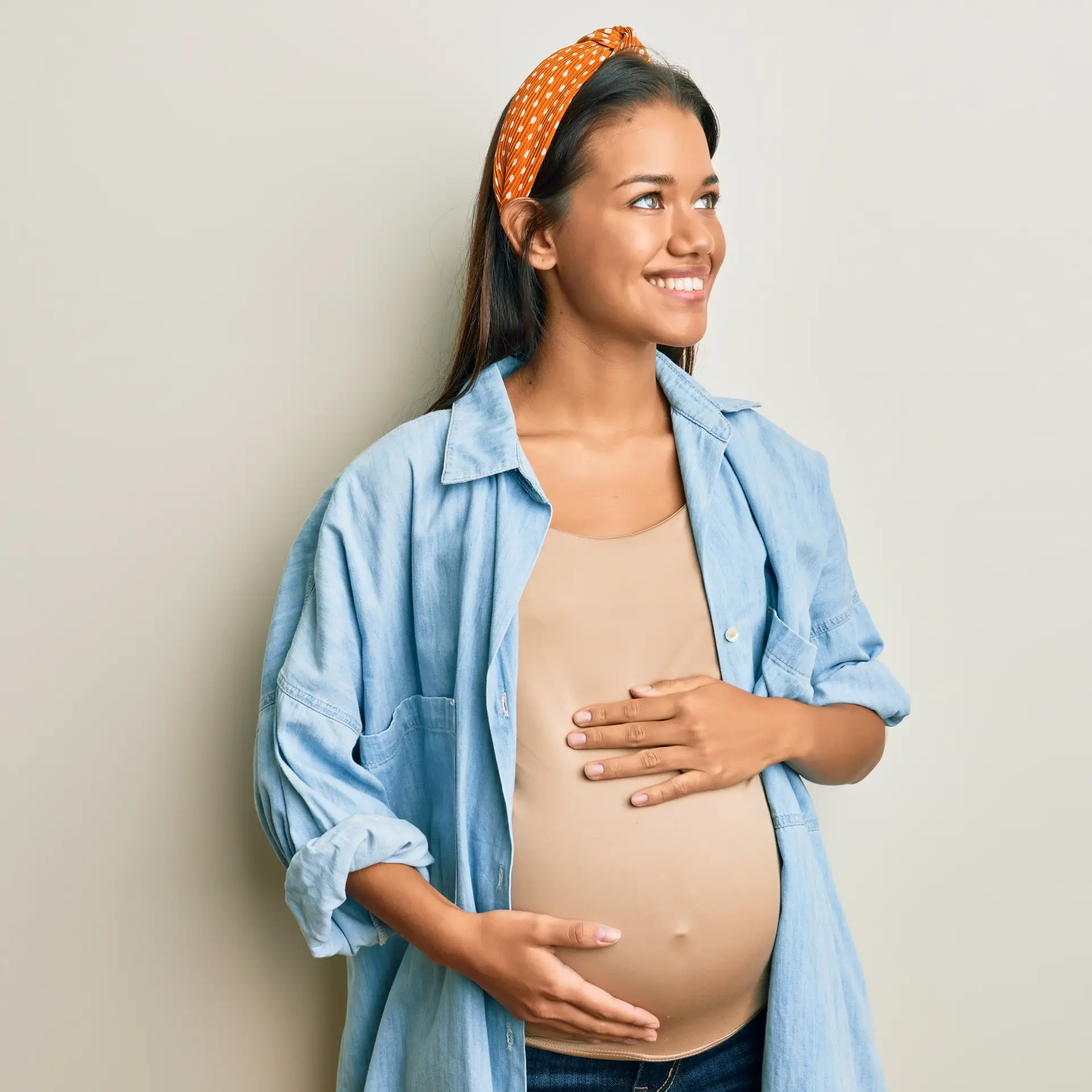 Beautiful hispanic woman expecting a baby, touching pregnant belly looking away to side with smile on face, natural expression. laughing confident.